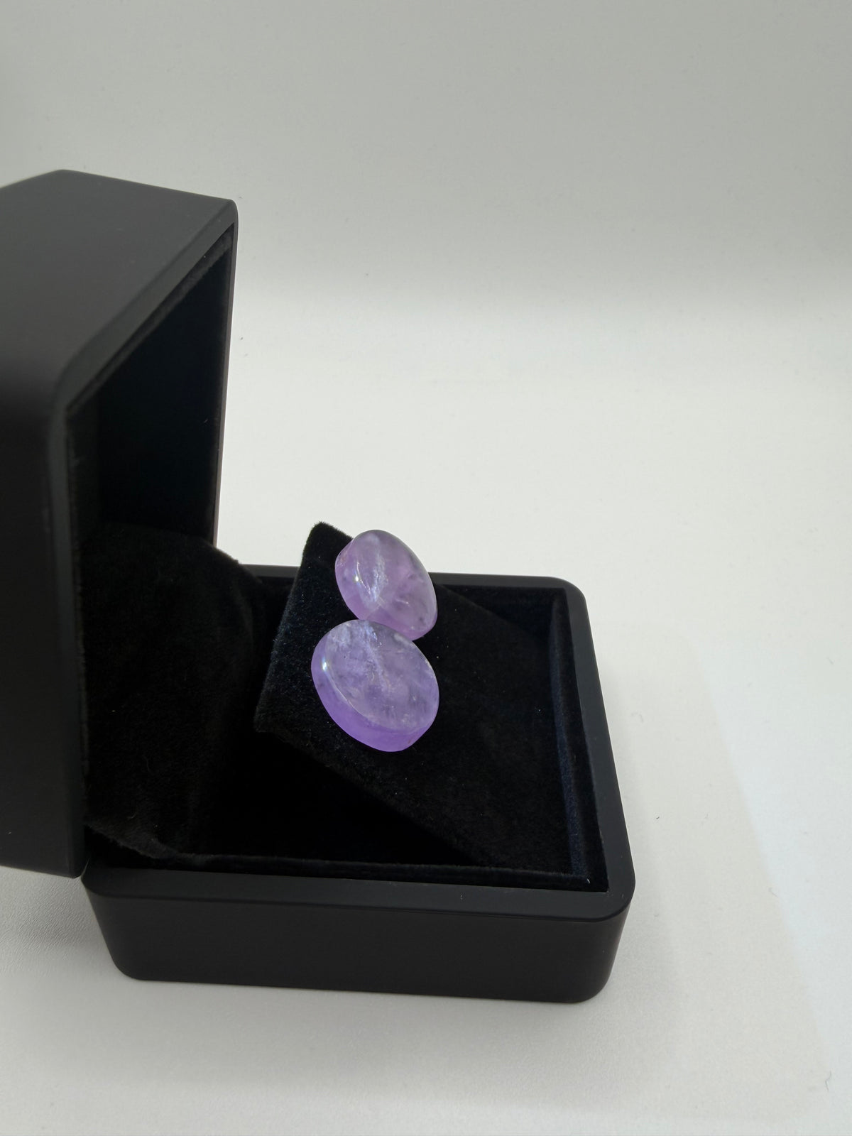 Angled view of polished lavender Rwandan amethyst cabochon earrings displayed in a black jewelry box.