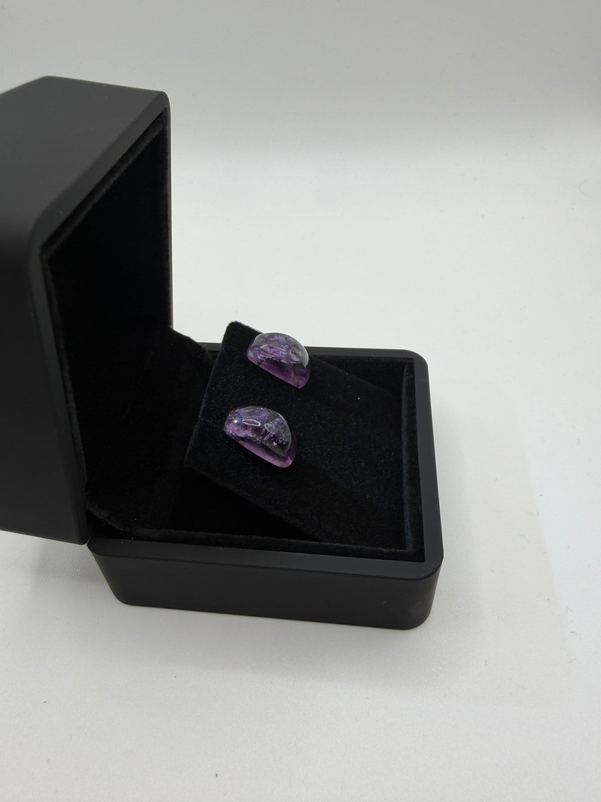 Side view of 14tcw Rwandan amethyst rectangular cabochon stud earrings in open black jewelry box, handcrafted in Maine