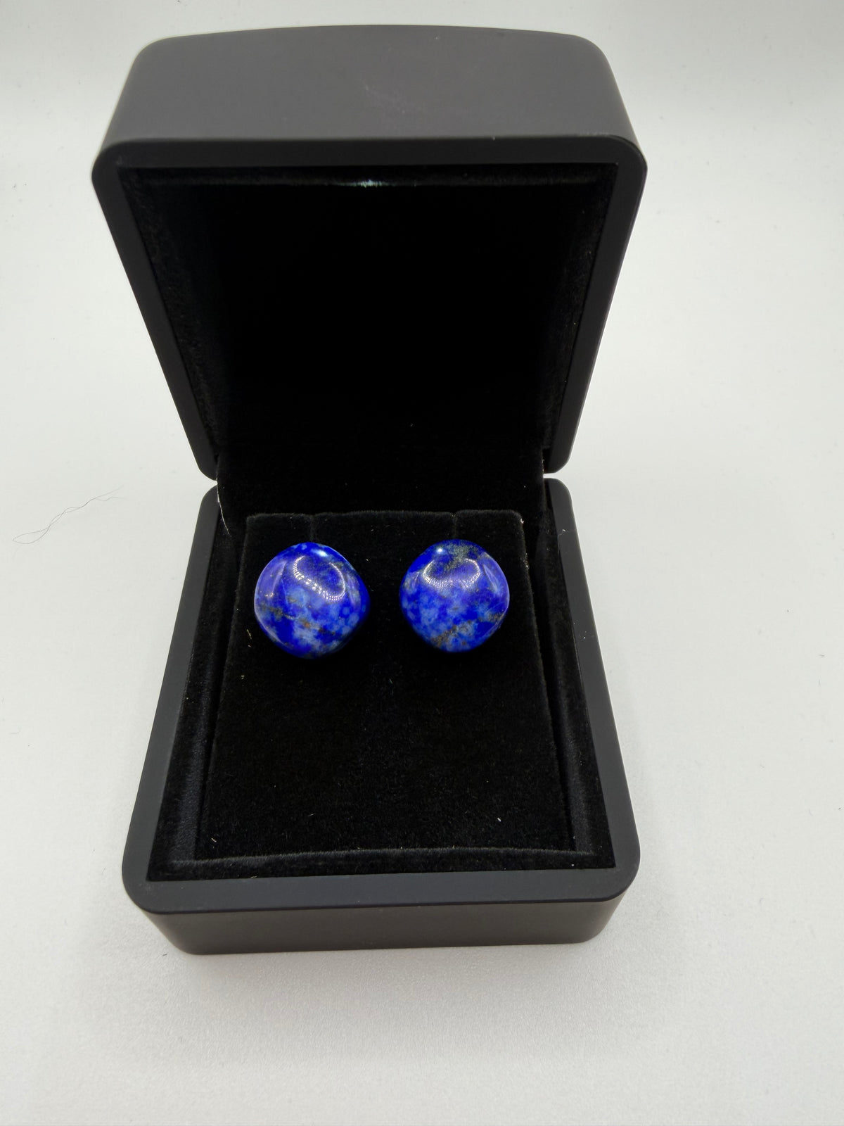 Top-down view of natural lapis lazuli stud earrings showing royal blue color, calcite clouds, and gold pyrite flecks in black jewelry box