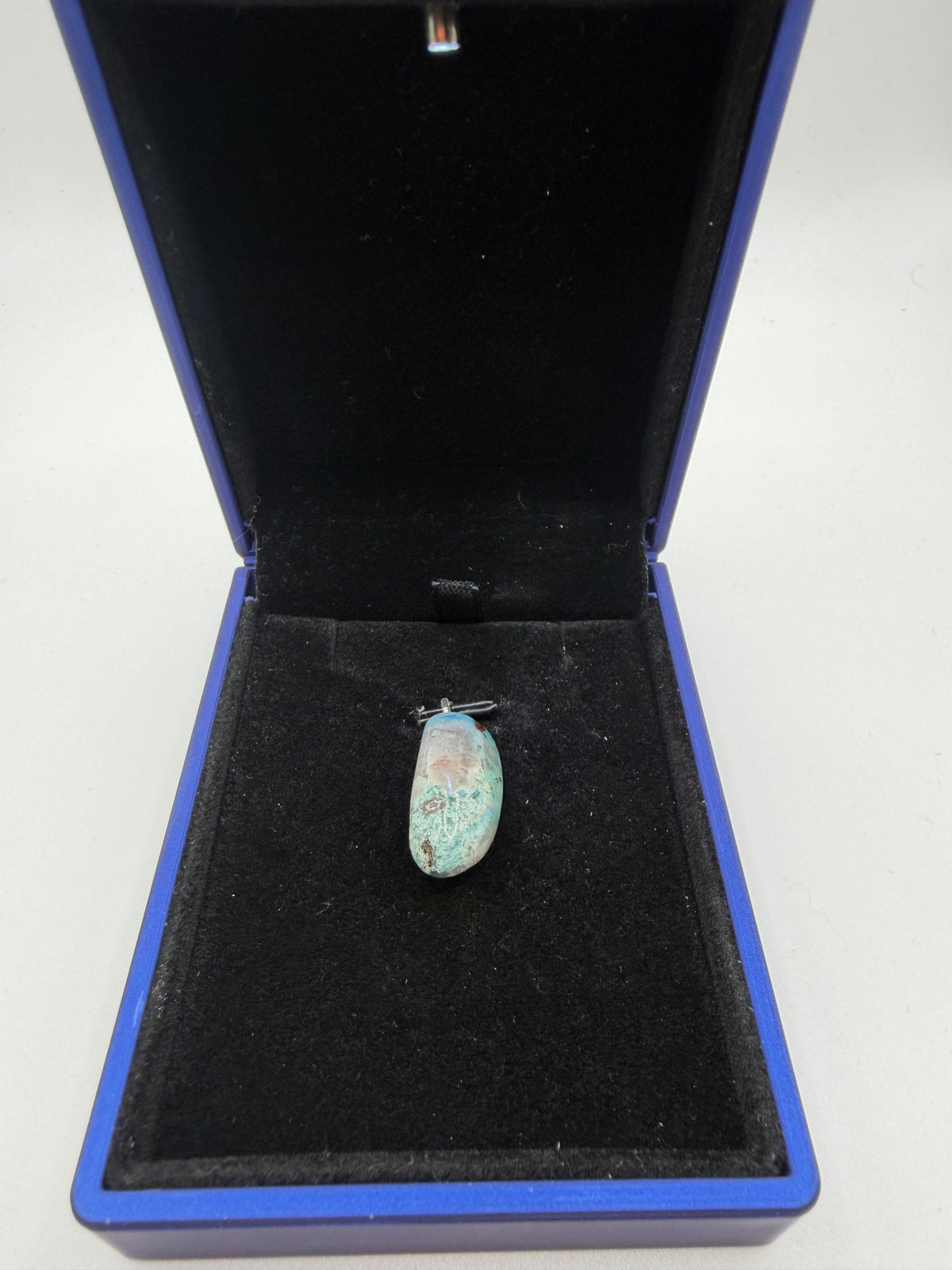 Top-down view of 18ct Namibian Quantum Quattro pendant in navy jewelry box, soft teal-blue with pale mineral matrix