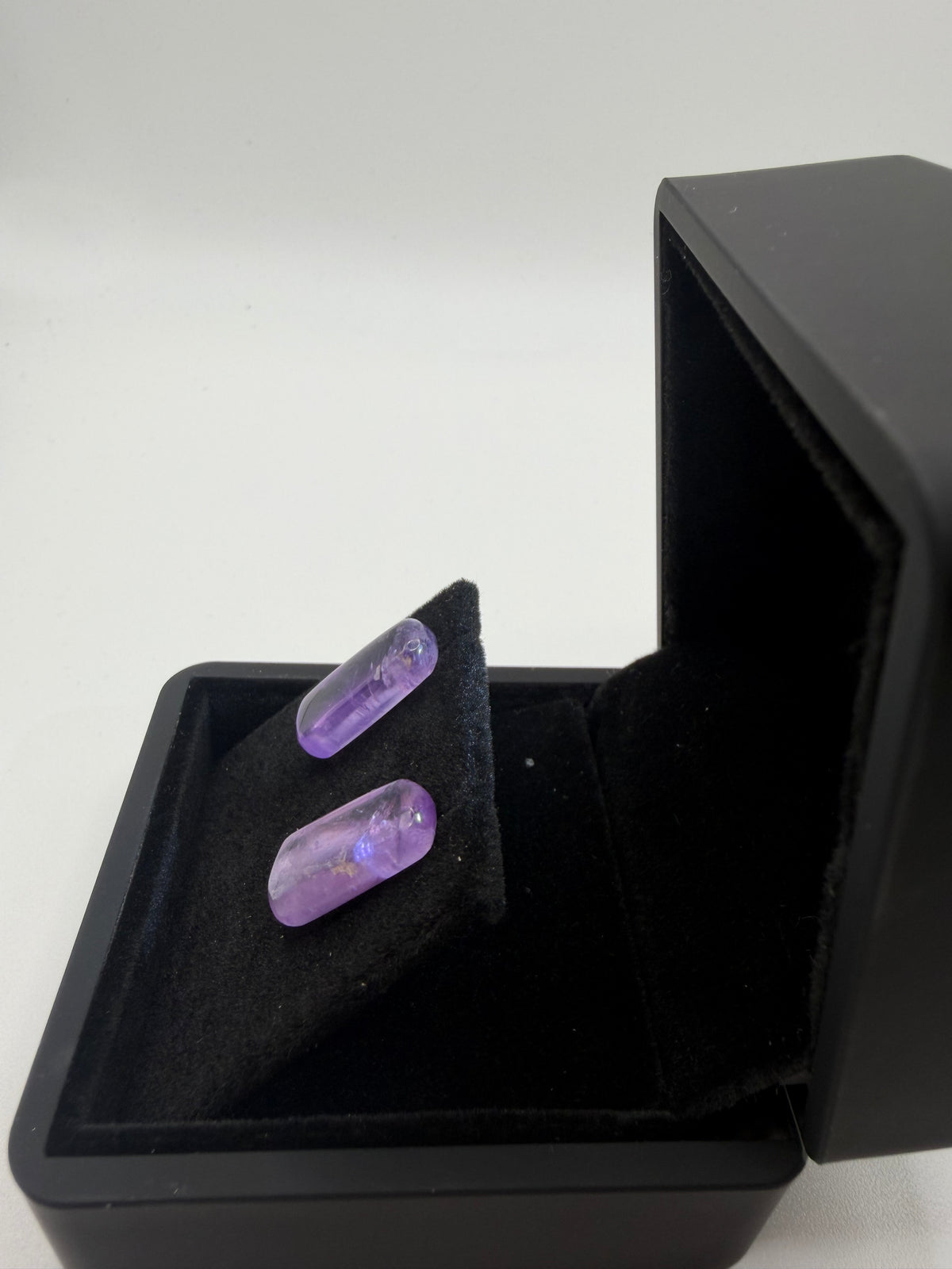 Angled view of 13 tcw Rwandan amethyst bar stud earrings with rounded corners and lavender-violet tones in a black jewelry box.