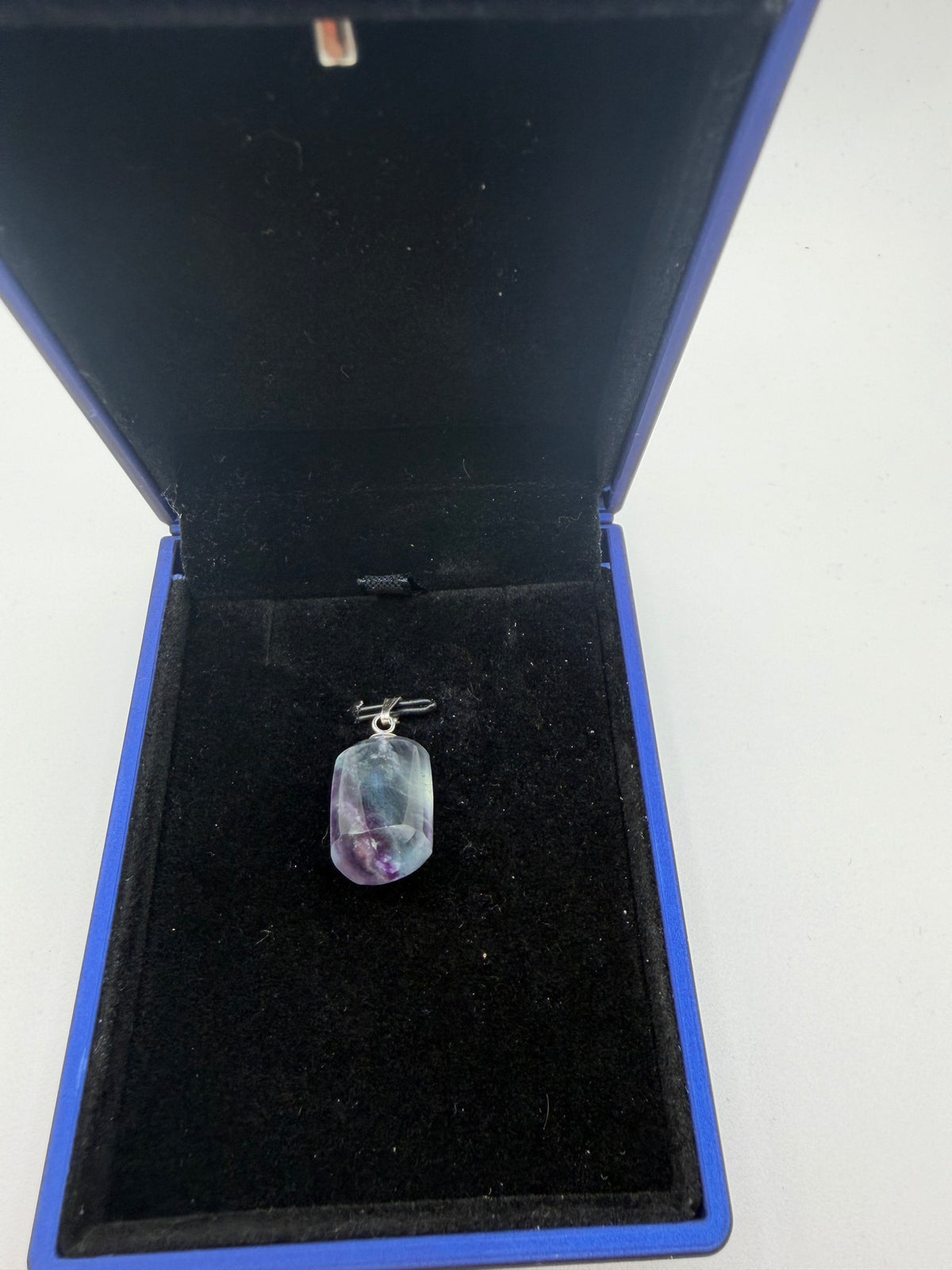 Top-down view of natural Namibian fluorite pendant in blue jewelry box, showing rectangular cabochon form and sterling silver bail