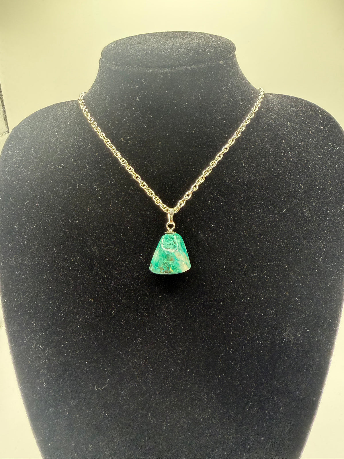 17ct teal-green Namibian Quantum Quattro pendant with sterling silver bail on a black bust; display chain not included.