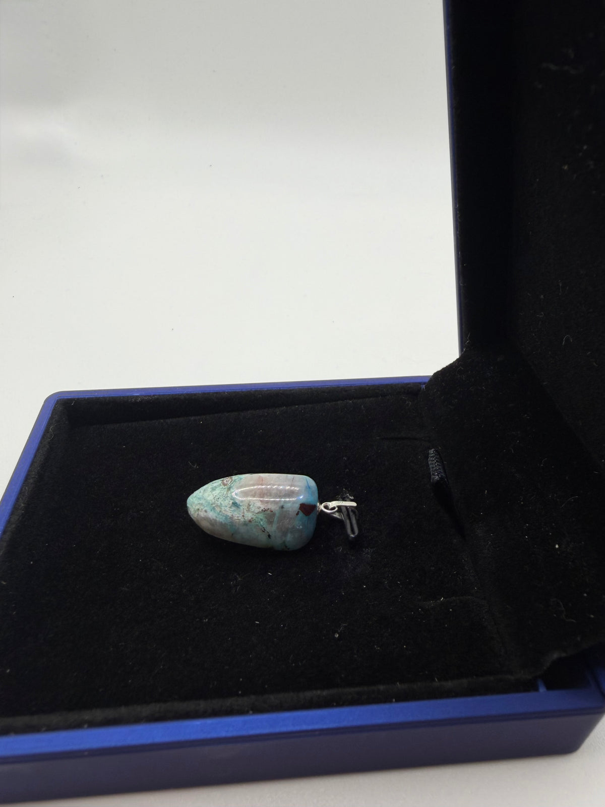Close-up angled view of natural Quantum Quattro pendant with sterling silver bail in open navy gift box, showing pale teal and matrix coloring