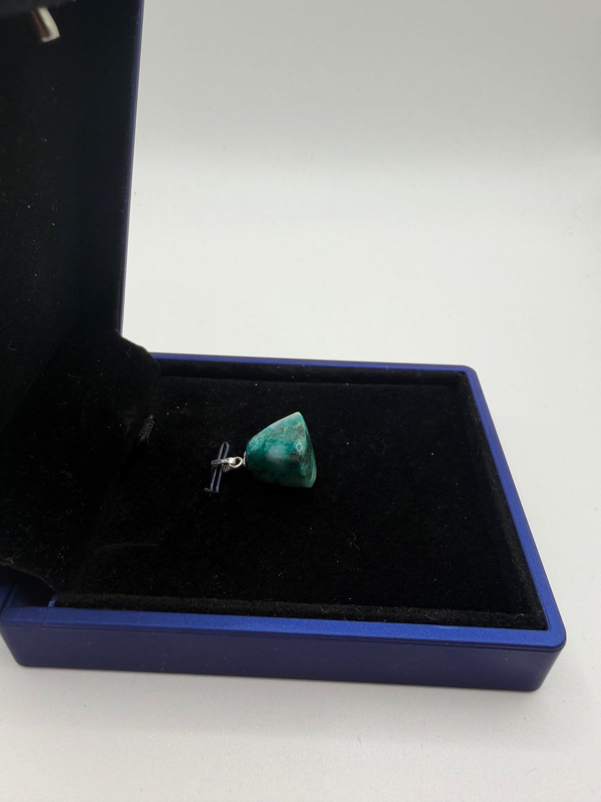 Angled view of 17ct Namibian Quantum Quattro pendant showing green color and pale patches in a blue jewelry box.