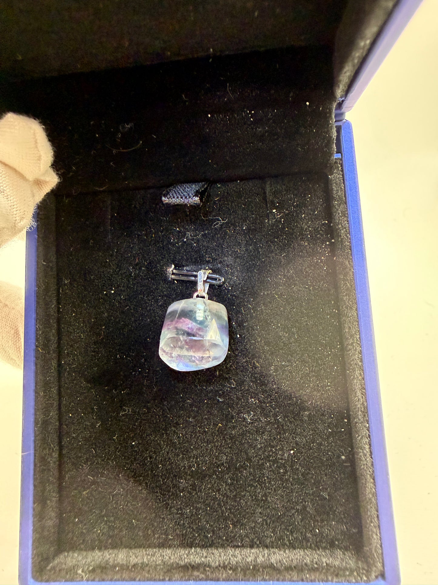 21ct Namibian fluorite pendant resting in open blue jewelry box, showing aqua and violet color zoning and sterling silver peg bail