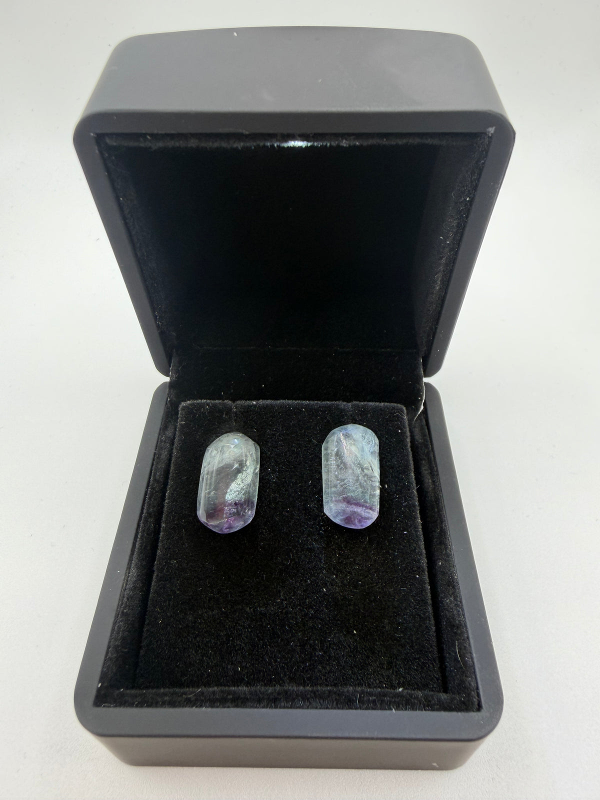 Top-down view of natural Namibian fluorite stud earrings showing violet-purple color zoning, displayed in open black jewelry box