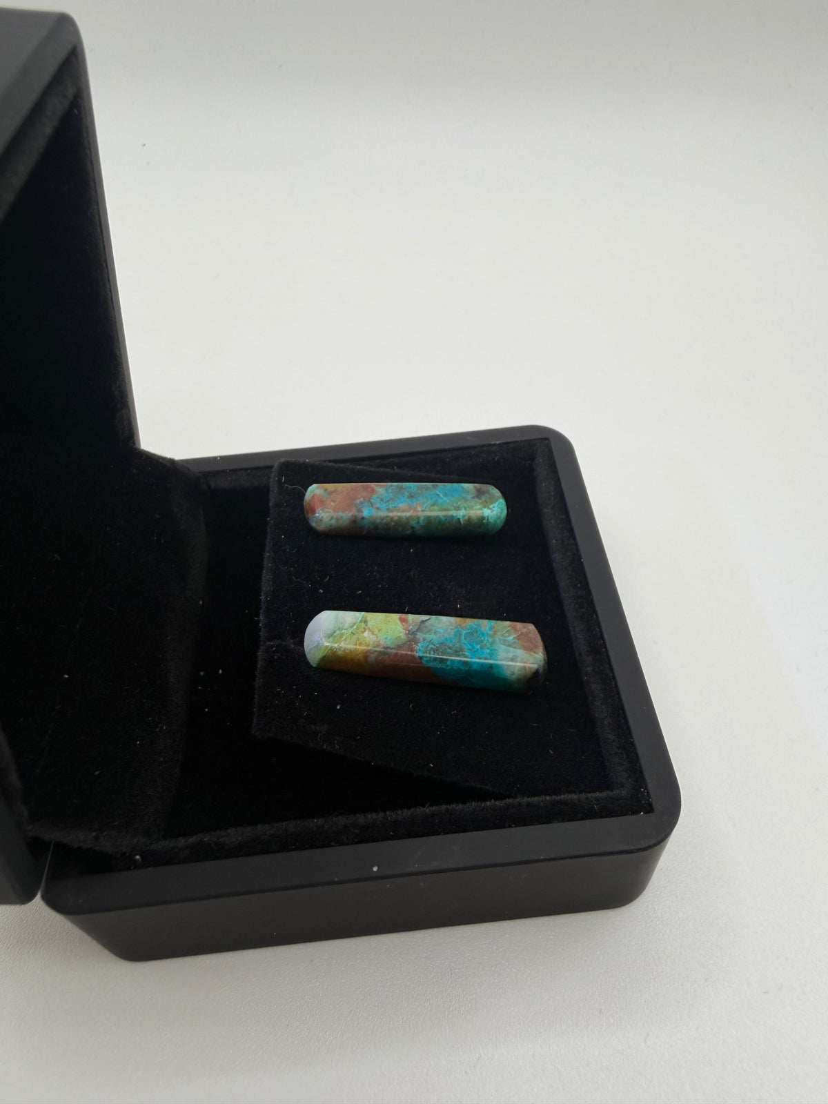 Angled view of natural Quantum Quattro bar stud earrings on titanium posts in black gift box, showing vivid multicolor matrix