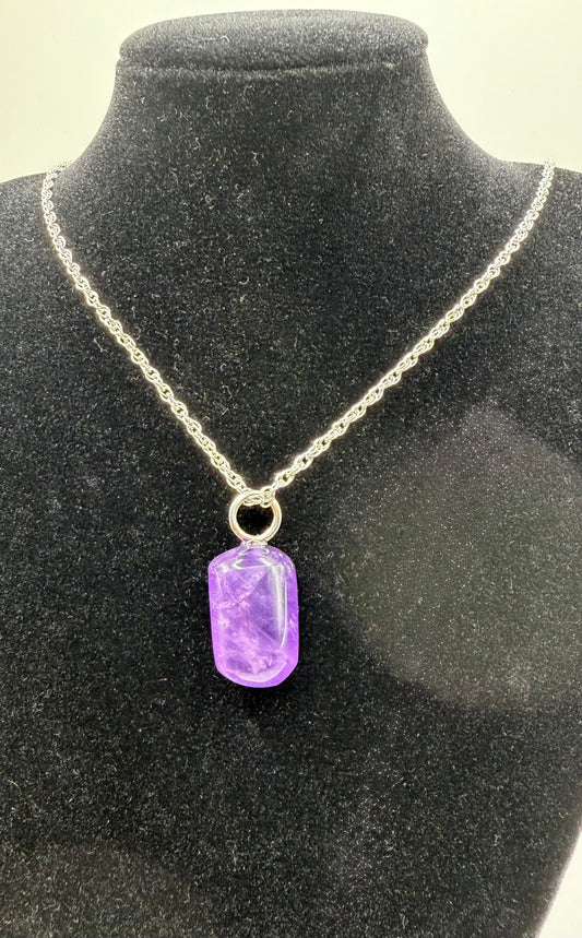 A silver chain necklace with a rectangular purple gemstone pendant, displayed on a black velvet jewelry bust.