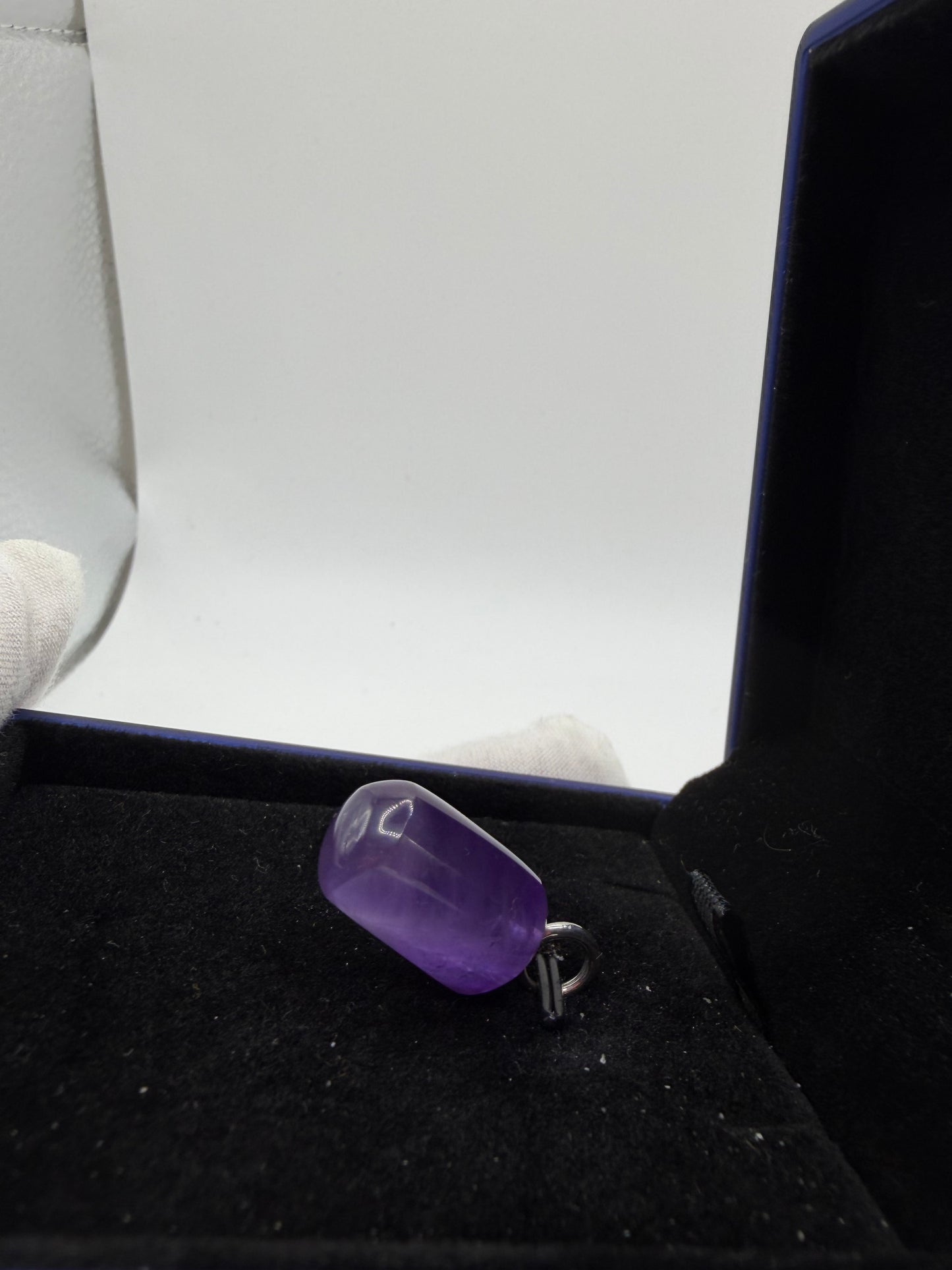 A polished purple gemstone pendant with a silver bail, displayed inside a black jewelry box.