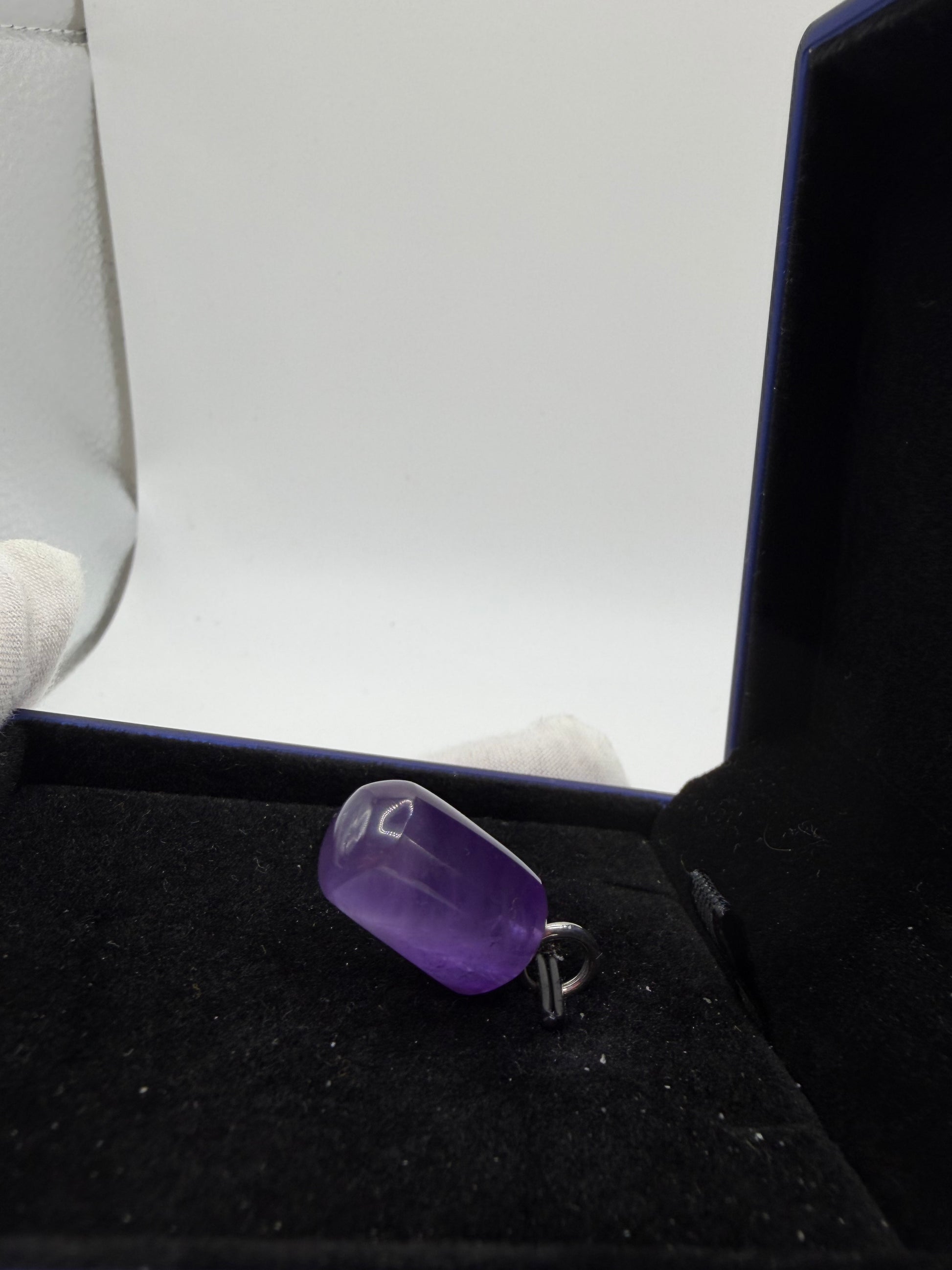 A polished purple gemstone pendant with a silver bail, displayed inside a black jewelry box.
