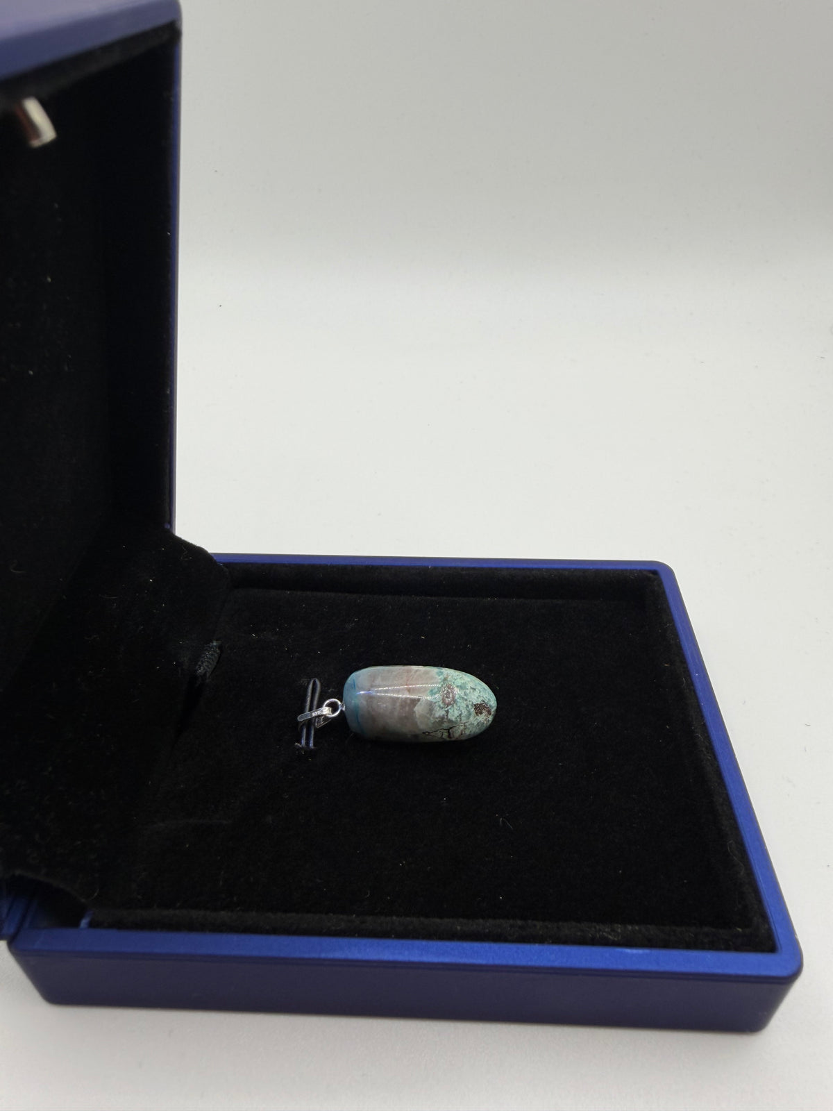 Side-angled view of compact rounded Quantum Quattro pendant in open navy gift box, sterling silver bail visible