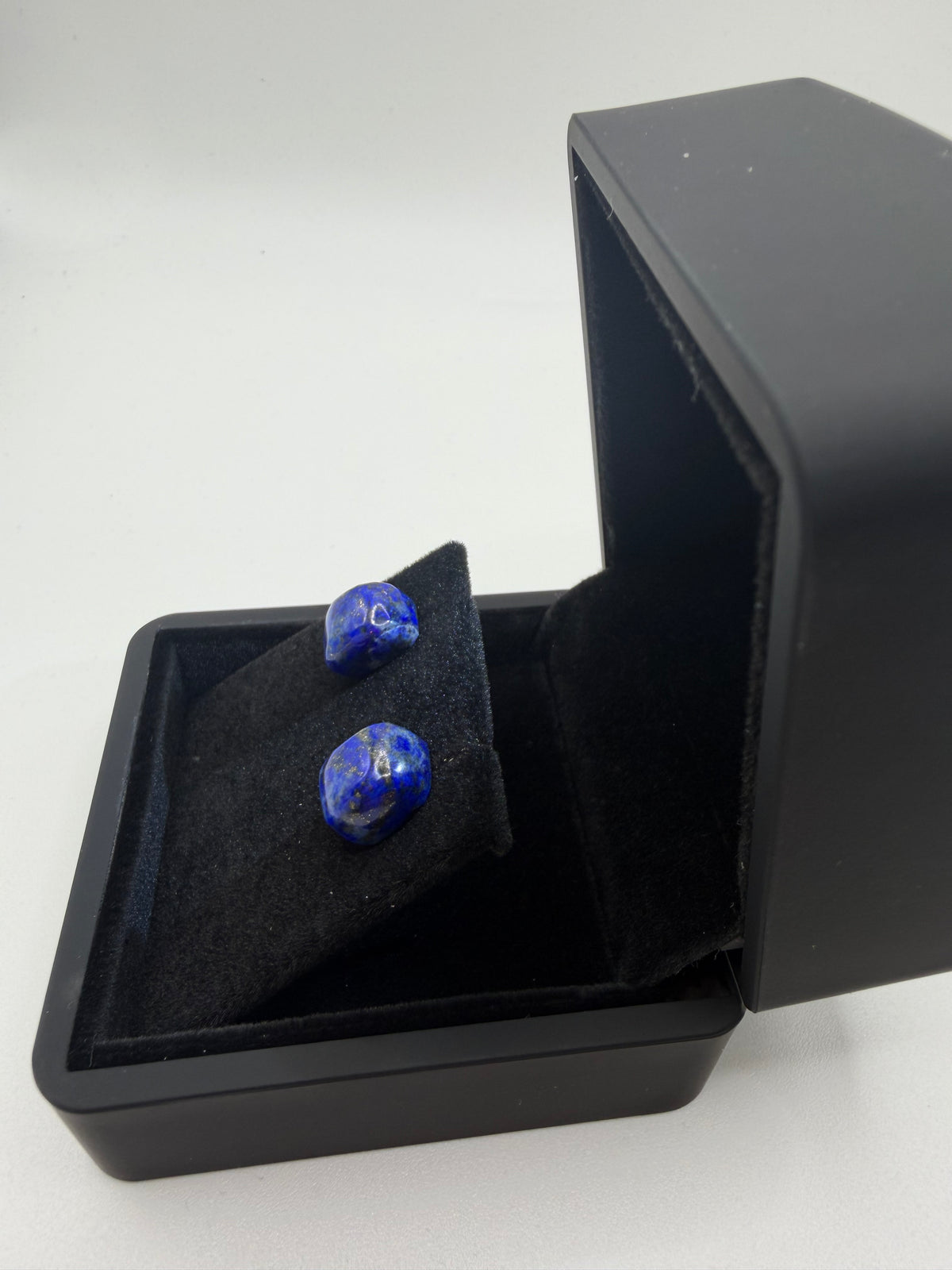 Angled view of lapis lazuli stud earrings on titanium posts in black gift box, showing deep blue color and gold pyrite flecks
