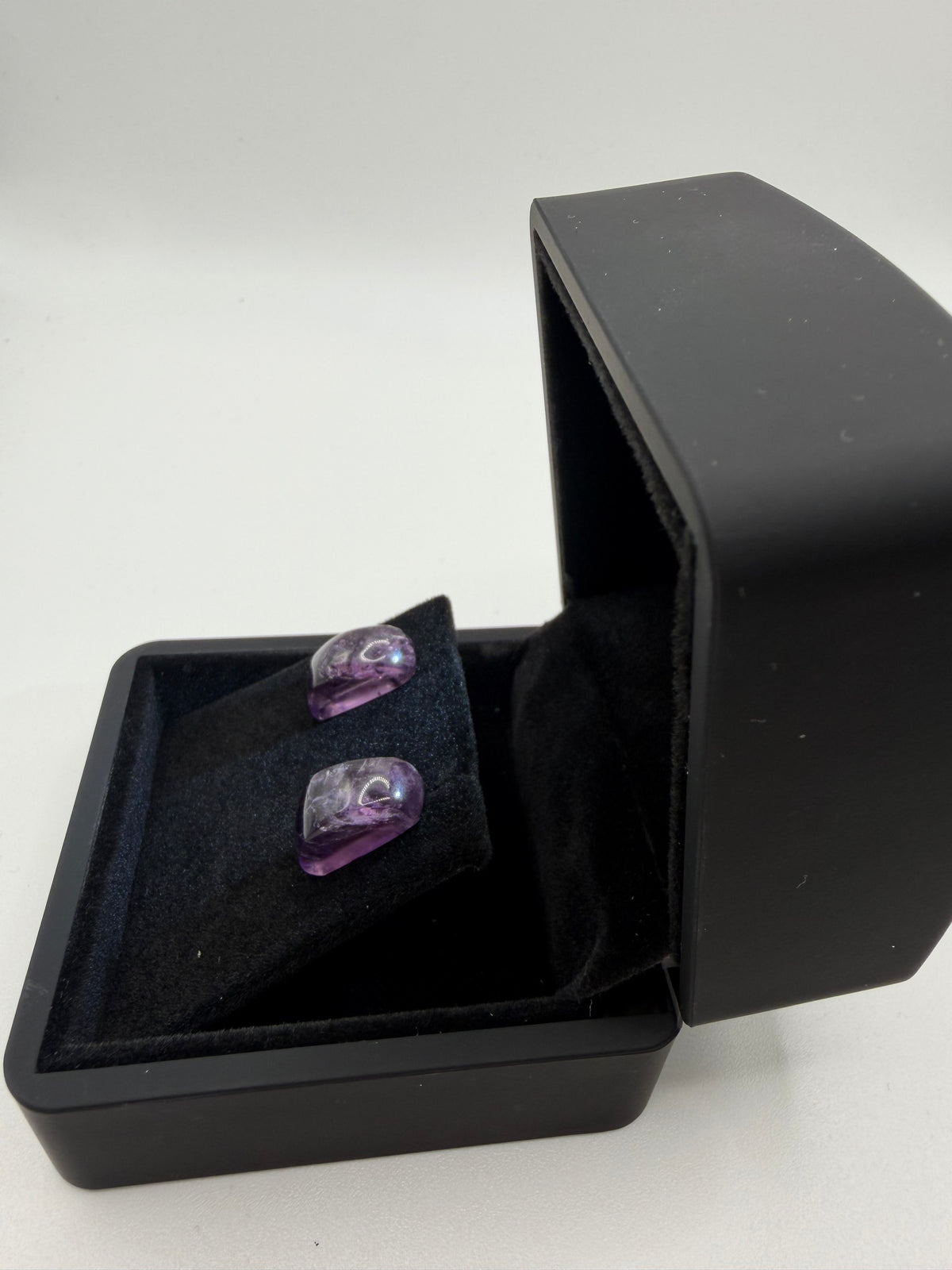 Angled view of natural Rwandan amethyst stud earrings on titanium posts in black gift box, showing translucent violet clarity