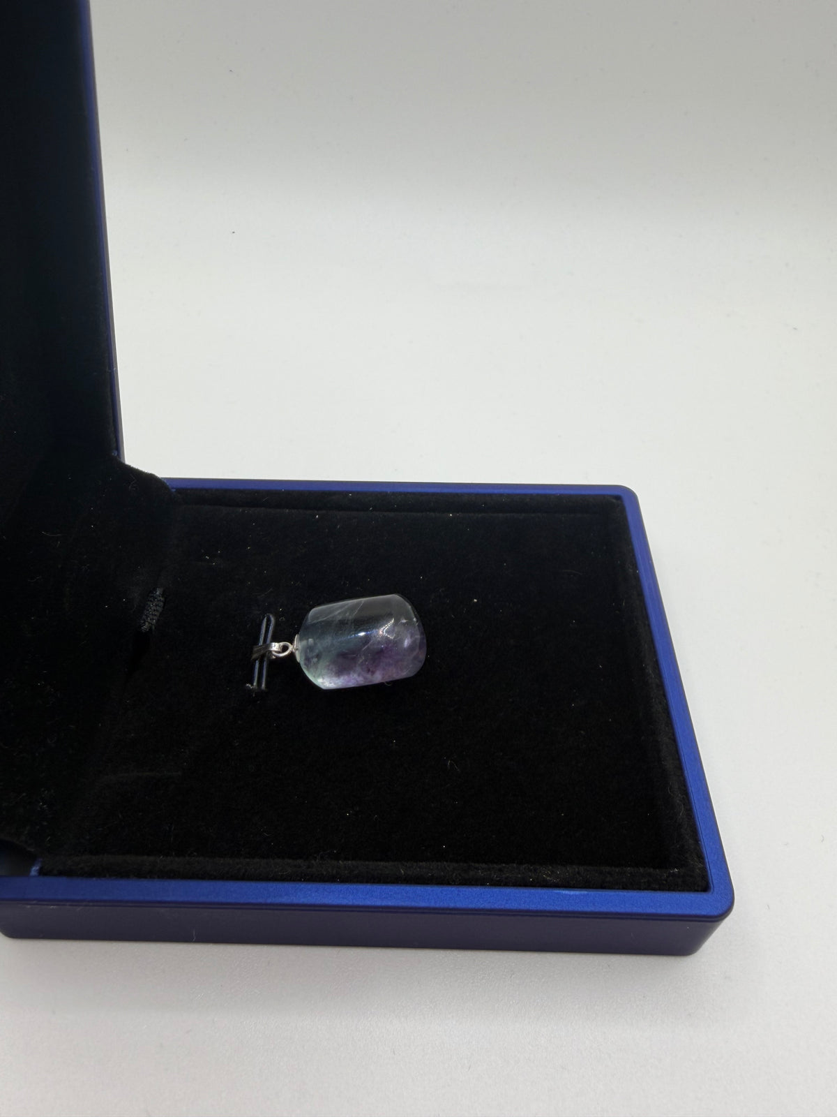 Side view of 25ct Namibian fluorite pendant in open blue jewelry box, near-colorless edges with violet-purple center band visible