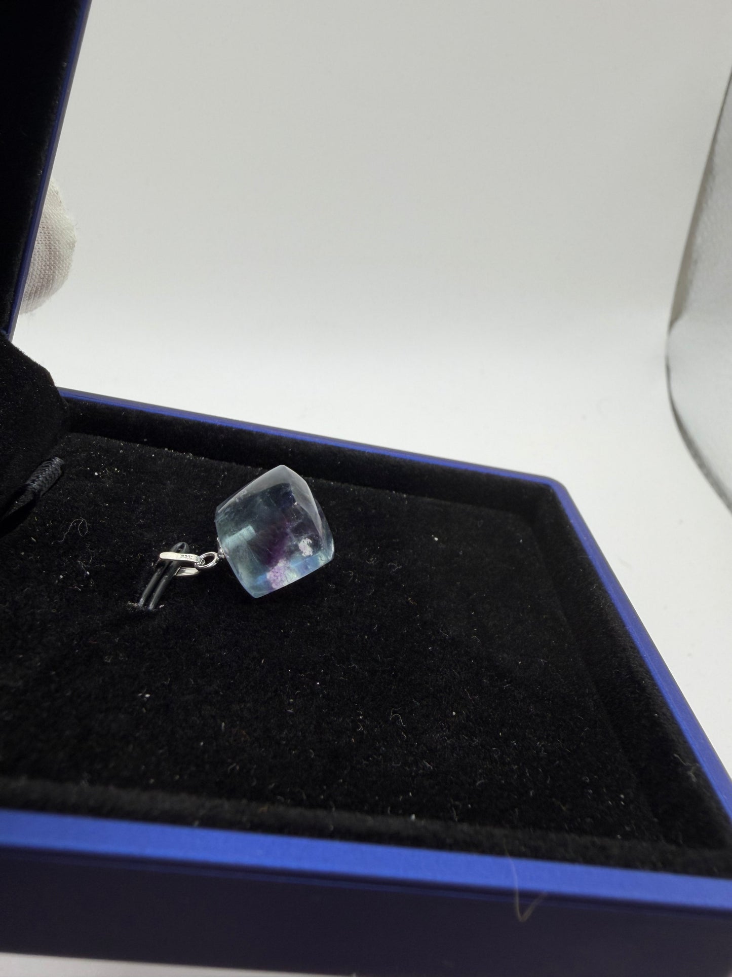 Side view of 21ct Namibian fluorite pendant in blue jewelry box, angled to show cube cut depth and sterling silver peg bail detail