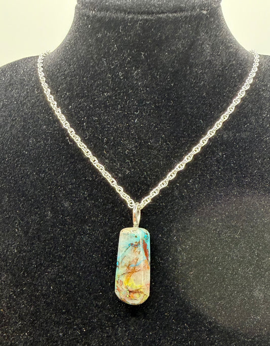 A silver chain necklace with a rectangular pendant featuring a marbled turquoise, gold, and brown pattern, displayed on a black velvet jewelry bust.