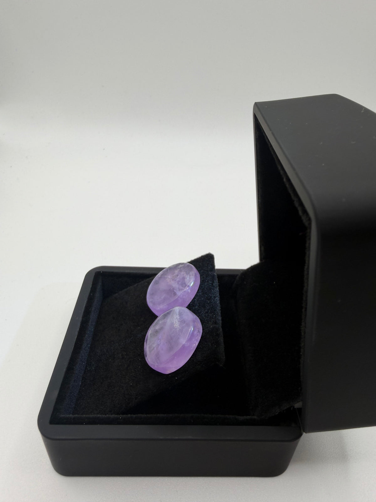 Side view of 26 tcw Rwandan amethyst cabochon stud earrings with pale lavender tones in a black jewelry box