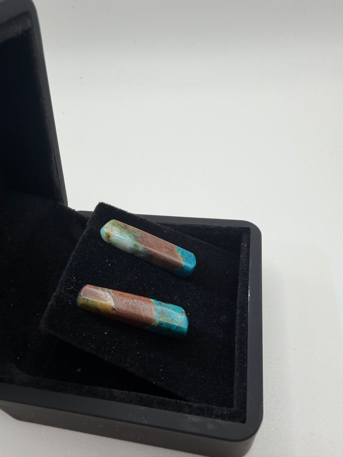 Angled view of Quantum Quattro bar stud earrings on titanium posts in black gift box, showing dramatic teal and terracotta color banding