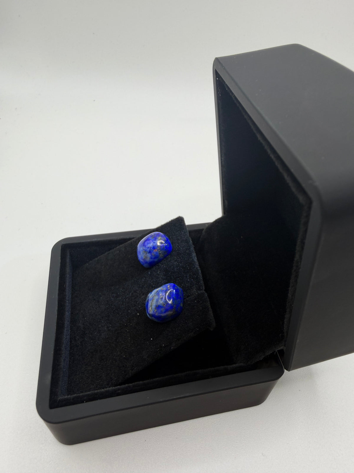 Angled view of lapis lazuli stud earrings on titanium posts in black gift box, showing deep blue color and gold pyrite veining